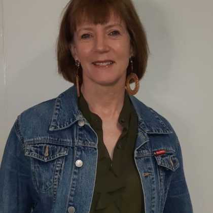 Dr Helena Donnelly smiles at the camera. she has short red hair and is wearing a denim jacket.
