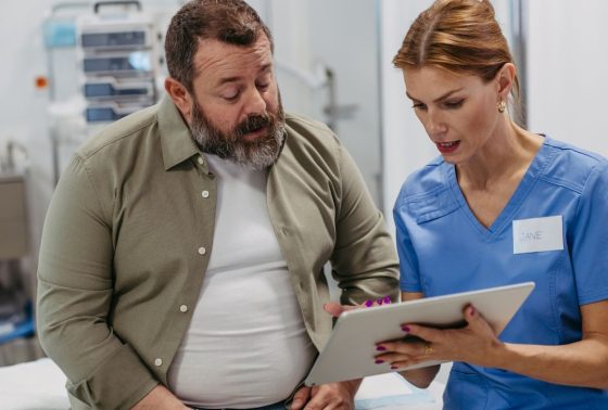 Female doctor consulting with overweight patient, discussing test result in doctor office. Obesity affecting middle-aged men's health. Concept of health risks of overwight and obesity.